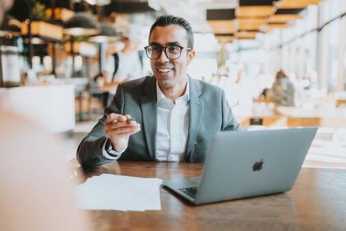 Mann mit MacBook im Café beim Gespräch