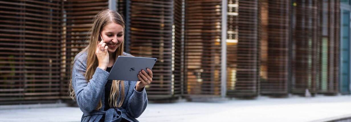 Frau mit iPad in der Hand und iPhone am Ohr