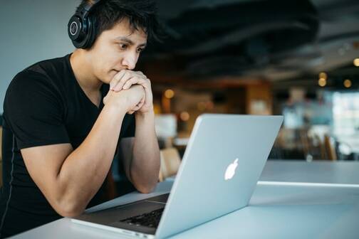 Mann sitzt mit Kopfhörer vor seinem MacBook