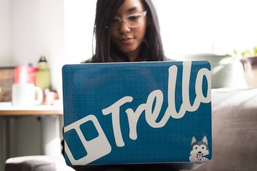 Trello ist eine nützliche Apps für To-dos Eine junge Frau sitzt hinter ihrem Mac mit Trello-Sticker